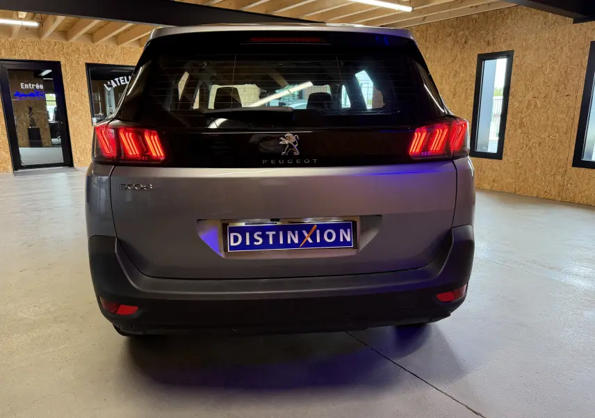 Vue arrière d’un Peugeot 5008 gris 2021 avec feux arrière allumés dans un garage lumineux.