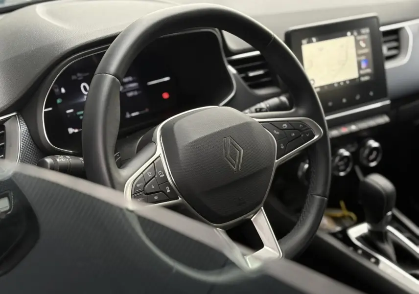 Vue rapprochée du volant noir et du tableau de bord numérique de la Renault Arkana 2025 avec écran tactile GPS.