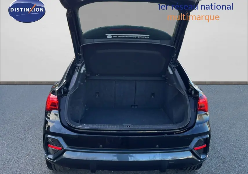 Vue arrière d’un Audi Q3 Sportback noir 2022 avec coffre ouvert et feux arrière allumés.