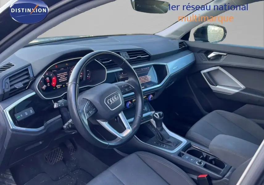 Intérieur de l'Audi Q3 Sportback 2022 vu côté conducteur, tableau de bord moderne avec écran tactile et volant cuir noir.