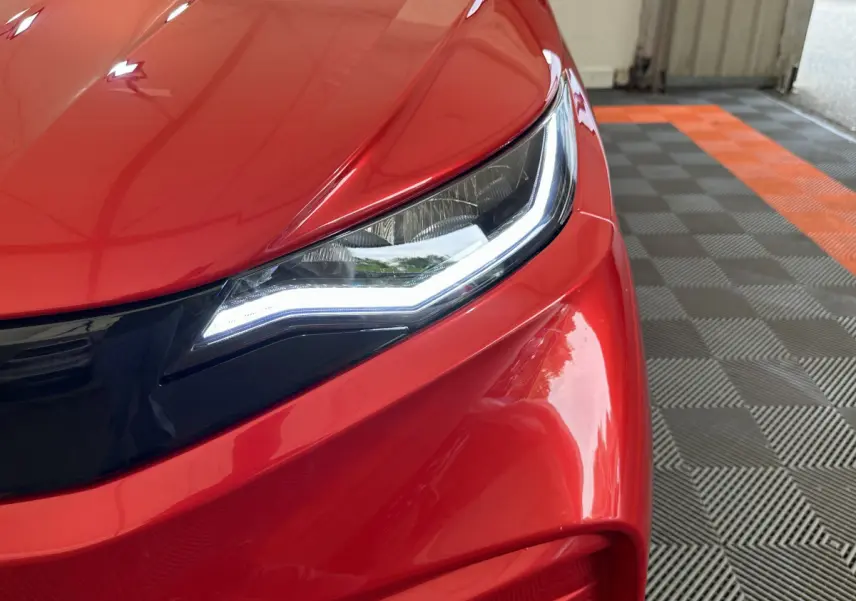 Gros plan sur le phare avant droit allumé d'une Aixam Ambition E City Pack rouge, soulignant ses lignes modernes.