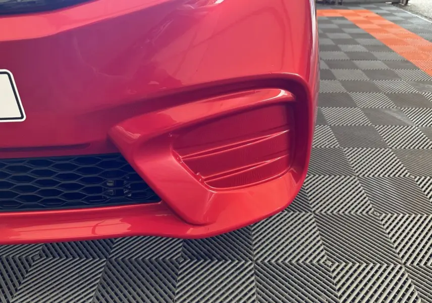 Gros plan sur le pare-chocs avant droit rouge de l'AIXAM AMBITION E CITY PACK 2026 avec grille noire et lignes sculptées.