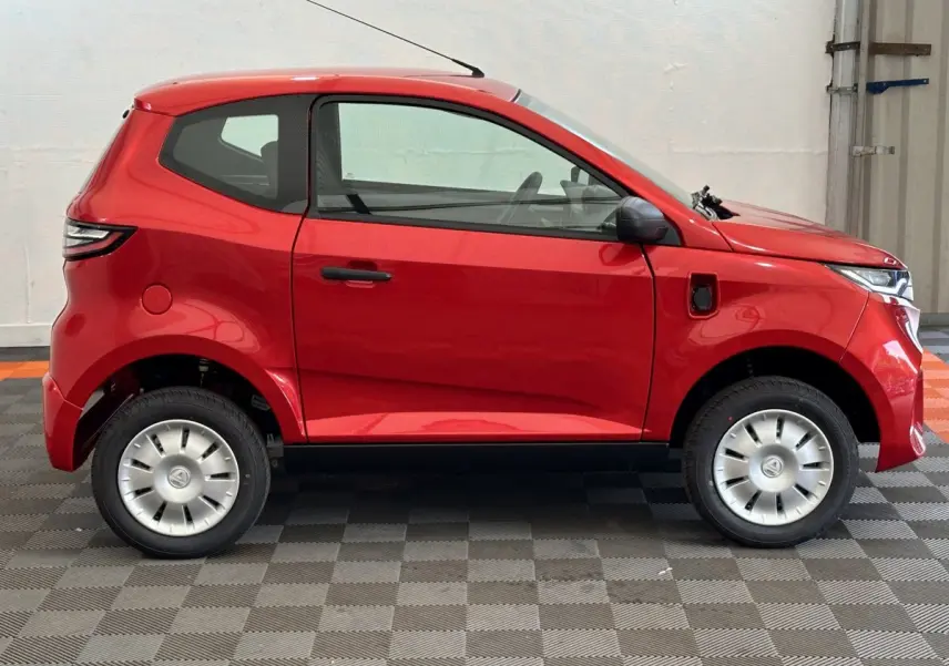 Vue de profil côté gauche d'une Aixam Ambition E City Pack rouge électrique avec rétroviseur caméra conducteur.