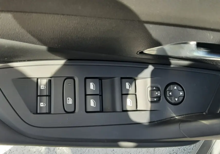 Vue rapprochée des commandes de lève-vitres et rétroviseurs sur la porte côté conducteur d'une Peugeot 308 gris selenium.