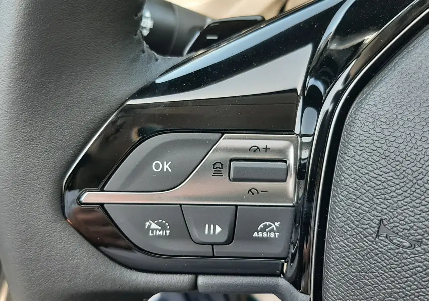 Gros plan sur les commandes noires du volant côté gauche du Peugeot 308 gris sélénium, boutons multifonctions visibles.