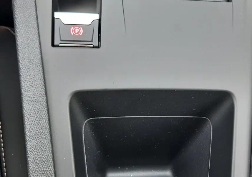 Gros plan sur la console centrale noire de la Peugeot 308 III Ph.2 avec bouton de frein à main électrique illuminé en rouge.