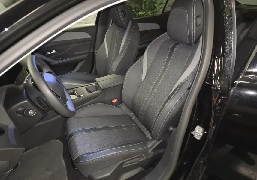 Vue intérieure côté conducteur du Peugeot 408 noir 2024, sièges tri-matières avec surpiqûres bleues et accoudoir central.