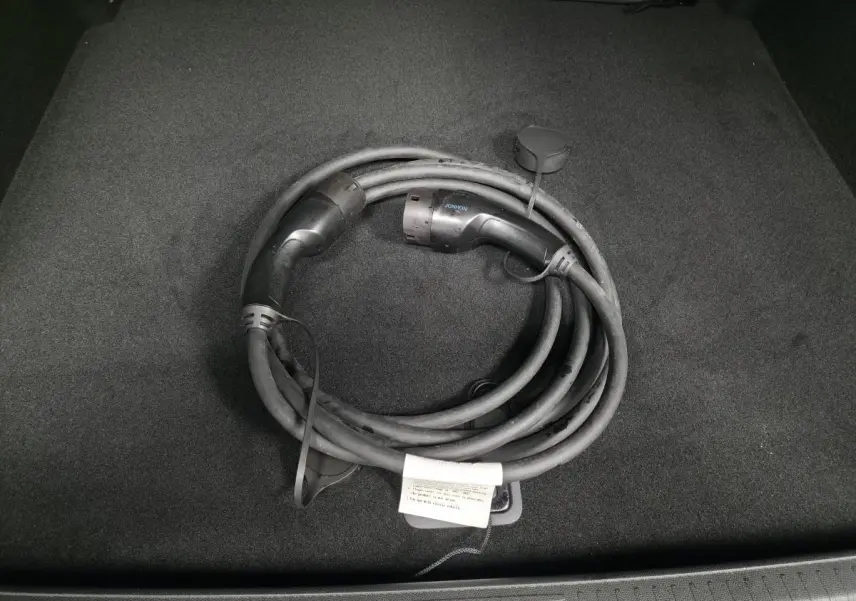 Câble de recharge électrique noir enroulé dans le coffre d'une Peugeot 408 E--210 Allure 2024.