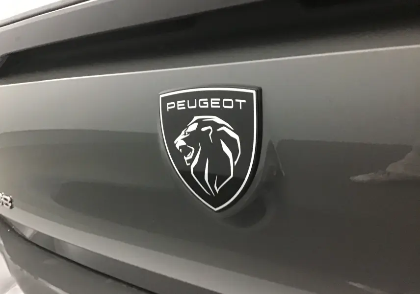 Gros plan sur le logo Peugeot noir et blanc sur la malle arrière d'une 308 gris Sellenium 2025.