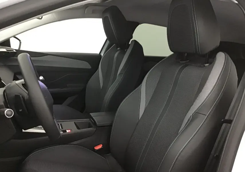Intérieur de la Peugeot 308 2025 vu côté conducteur, sièges en tissu noir et gris avec surpiqûres blanches.