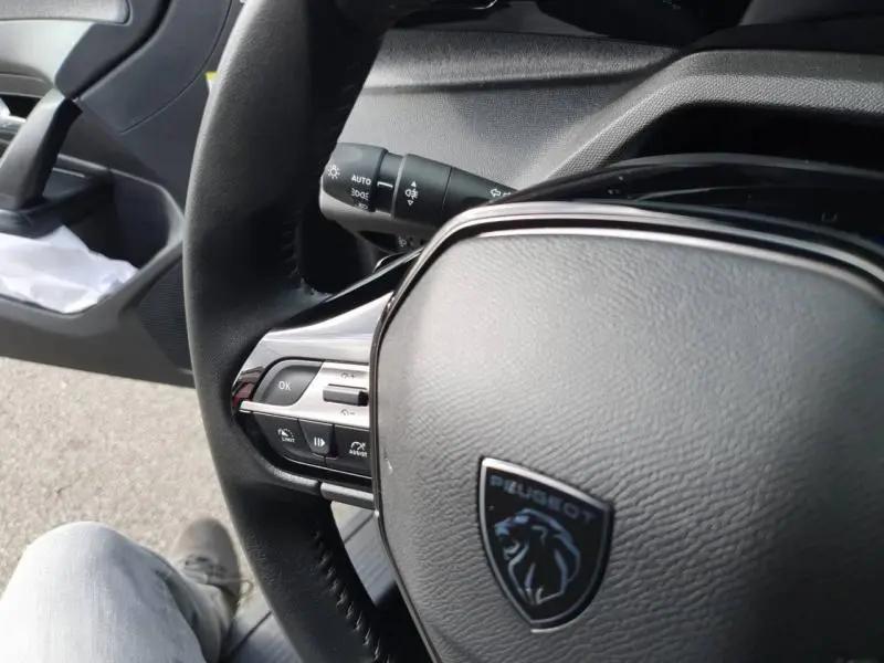 Gros plan sur le volant multifonction noir avec logo Peugeot, côté gauche, intérieur de la 308 gris Sélénium.