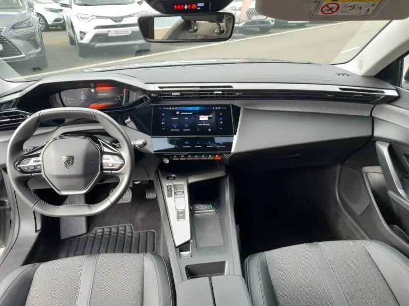 Vue intérieure avant de la Peugeot 308 2024 gris Sélénium, tableau de bord moderne avec écran tactile et volant multifonction.