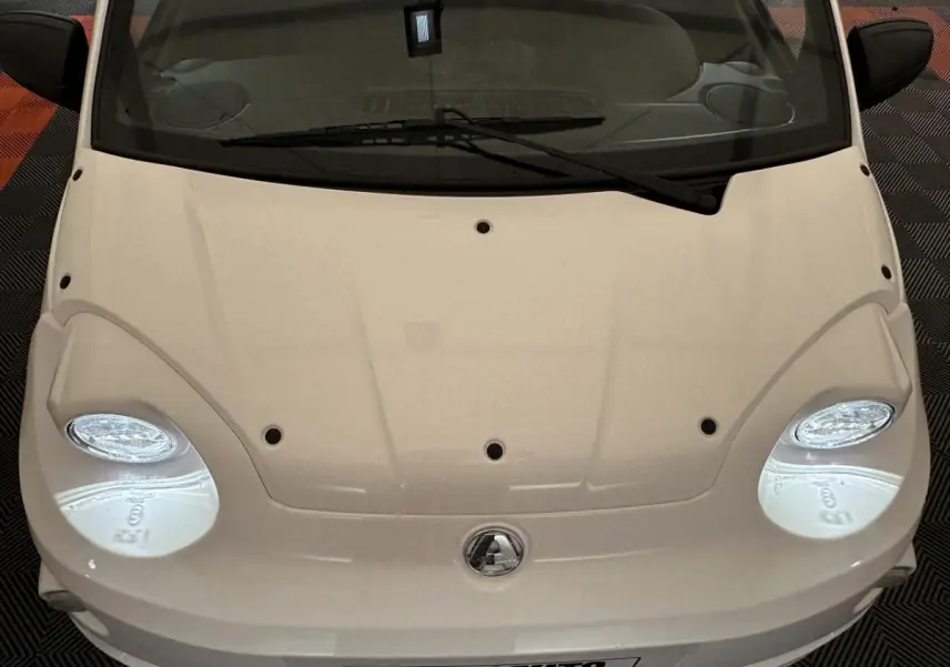 Vue plongeante avant d'une Aixam Minauto E Access blanche, mettant en valeur ses phares ronds et son capot épuré.