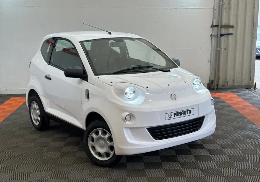 Vue 3/4 avant droite d'une Aixam Minauto E Access blanche avec phares ronds et rétroviseur caméra côté conducteur.