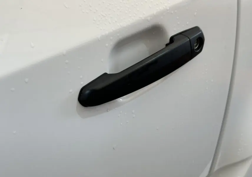 Poignée de porte noire en gros plan sur la portière blanche d'une Aixam Minauto E Access 2026, côté conducteur.