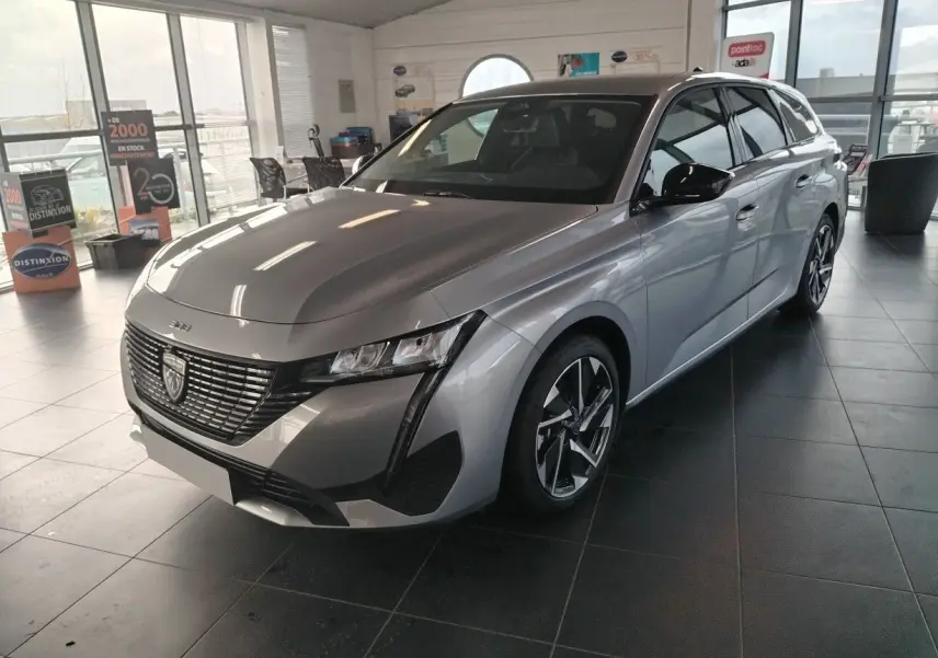 Peugeot 308 SW Hybrid gris Artense vue 3/4 avant droit en showroom avec jantes bi-ton et calandre distinctive.