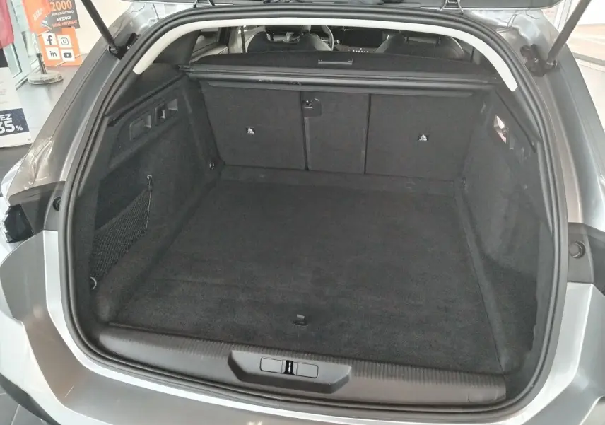 Coffre ouvert vu de l'arrière d'une Peugeot 308 SW Hybrid 145 gris Artense, montrant un espace de chargement spacieux et propre.
