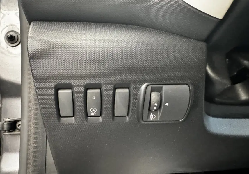 Gros plan sur les commandes de réglage des phares et désactivation du démarrage automatique, intérieur Renault Twingo gris foncé.