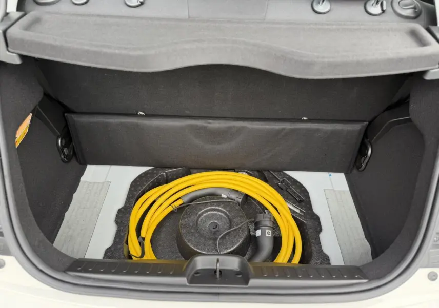 Coffre ouvert d'une FIAT 500 électrique blanc Artic, montrant le câble de recharge jaune rangé dans l'espace sous la tablette arrière.