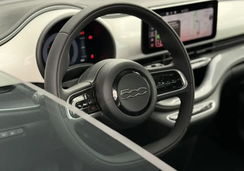 Intérieur de la Fiat 500 électrique 2024, vue centrée sur le volant noir Soft-Touch et planche de bord blanche Artic.