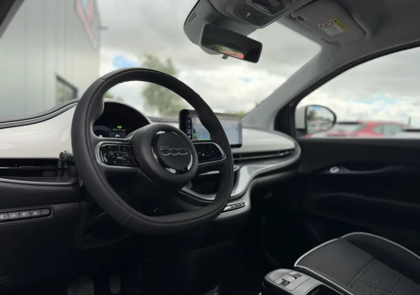 Intérieur de la Fiat 500 électrique 2024 vu côté conducteur, volant noir soft-touch et planche de bord blanc Artic.