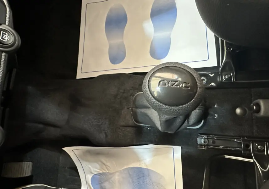 Vue intérieure centrée sur le levier de vitesse automatique noir avec logo Aixam, entouré de tapis de sol noirs.