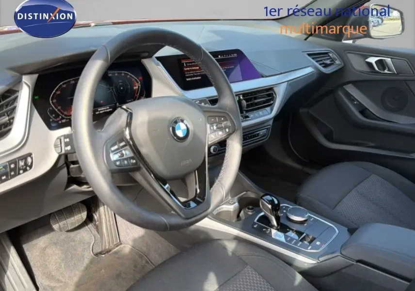 Vue intérieure côté conducteur de la BMW Série 1 116i 2022, volant cuir, console centrale avec boîte auto et écran tactile.