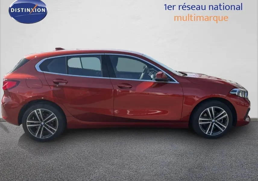 Profil latéral droit d'une BMW Série 1 116i Business 2022 en orange Sunset métallisé, avec jantes alliage et vitres teintées.