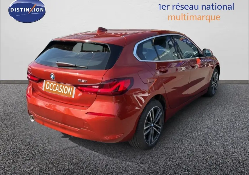 Vue 3/4 arrière droite d'une BMW Série 1 116i Business en orange Sunset métallisé avec jantes alliage et feux LED.