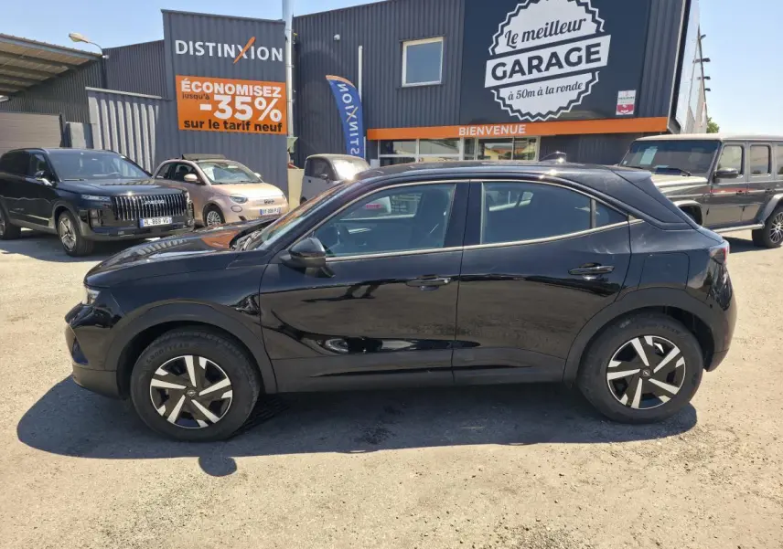 Opel Mokka noir vue de profil côté gauche, avec jantes bicolores et toit couleur carrosserie, stationné devant un garage.