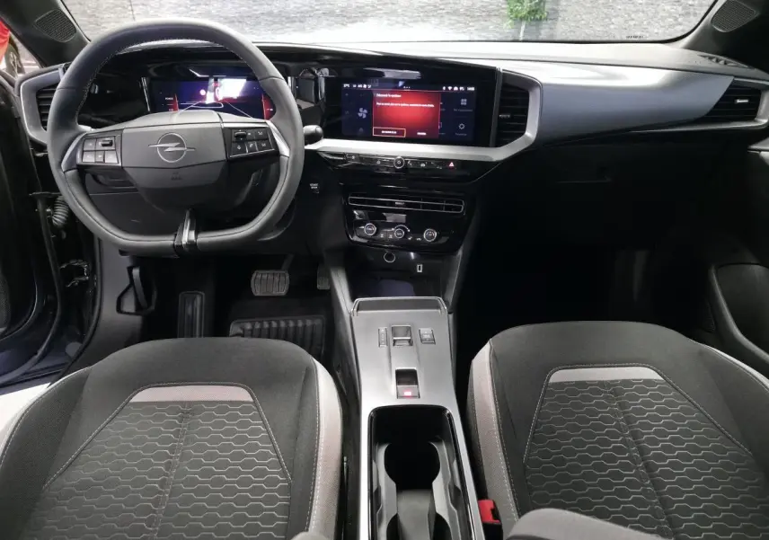 Vue intérieure avant de l'Opel Mokka 2025, tableau de bord noir avec écran tactile 10 pouces et sièges tissu gris à motifs.