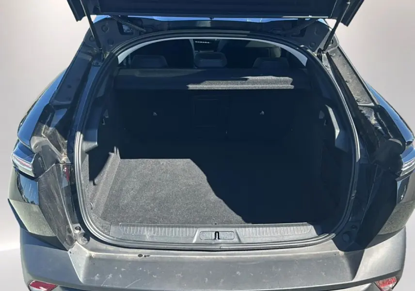 Coffre ouvert vu de l'arrière d'une Peugeot 408 Hybrid 145 allure e-dcs6 noire, montrant l'espace de chargement vide.