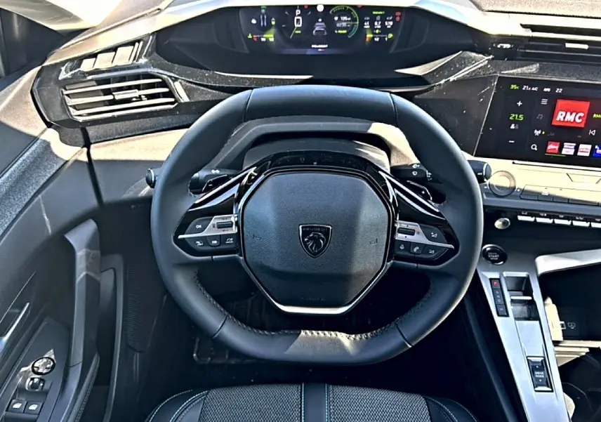 Vue intérieure centrée sur le volant cuir noir et le tableau de bord numérique de la Peugeot 408 Hybrid 145 allure 2025.
