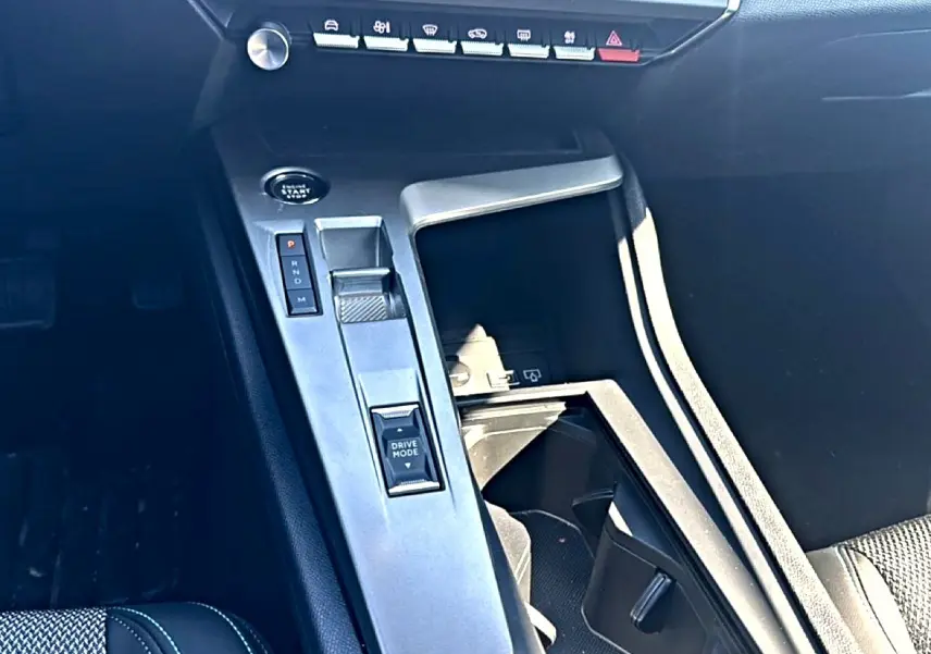 Vue intérieure centrée sur la console centrale noire du Peugeot 408 Hybrid 145 allure avec sélecteur de boîte auto et bouton Drive Mode.
