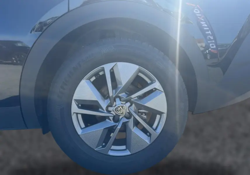 Gros plan sur la jante alu avant droite noire du Peugeot 408 Hybrid 145 allure e-dcs6 avec logo central Peugeot.