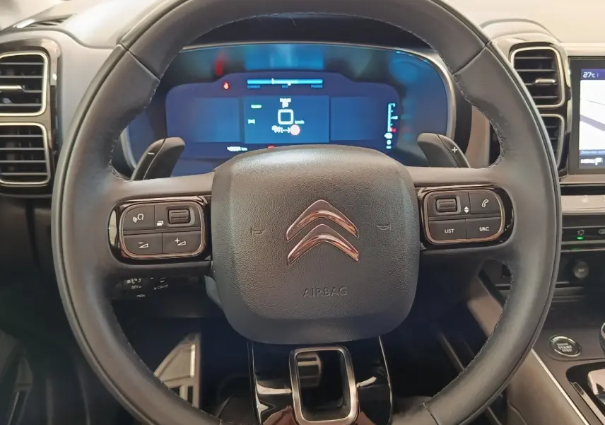 Vue rapprochée du volant cuir multifonctions du Citroën C5 Aircross Hybrid 225 ë-EAT8 avec tableau de bord numérique en arrière-plan.