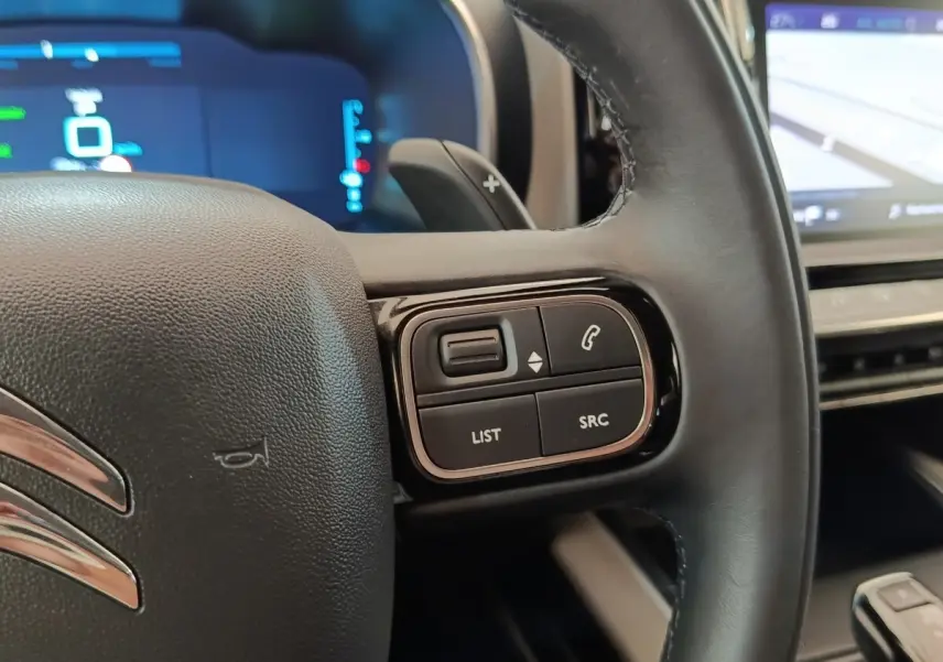 Gros plan sur le volant cuir noir du Citroën C5 Aircross Hybrid 225 ë-EAT8 avec commandes audio et écran tactile de navigation visible.