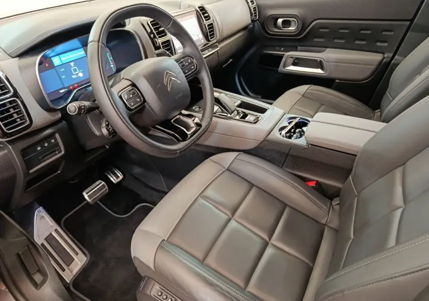 Vue intérieure côté conducteur du Citroën C5 Aircross Hybrid gris foncé, avec volant cuir et tableau de bord digital.