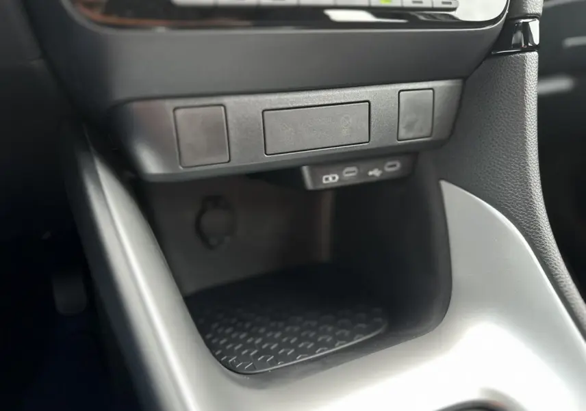 Gros plan sur la console centrale noire et grise de la Toyota Yaris 2025 Hybride avec ports USB-C et rangement antidérapant.