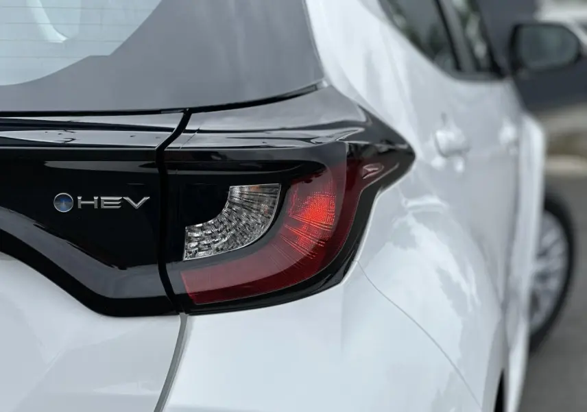 Gros plan sur le feu arrière droit et l'inscription HEV d'une Toyota Yaris hybride blanche vue de l'arrière.