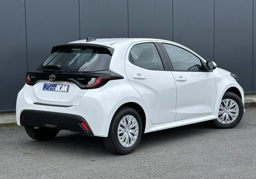 Vue 3/4 arrière droite d'une Toyota Yaris hybride blanche avec toit noir et jantes acier à enjoliveurs.