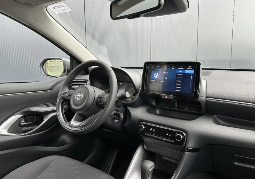 Vue intérieure côté conducteur de la Toyota Yaris 2025 hybride, avec tableau de bord noir et écran tactile central allumé.
