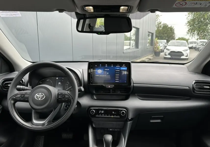 Vue intérieure avant de la Toyota Yaris blanche 2025, tableau de bord moderne avec écran tactile et volant multifonction en cuir.