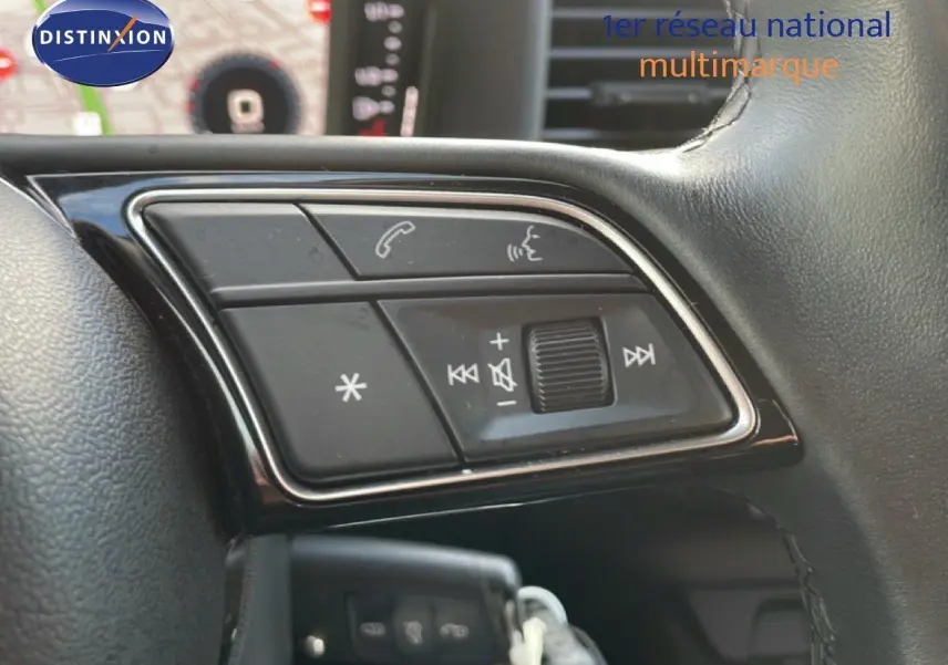 Gros plan sur les commandes audio et téléphone intégrées au volant noir de l'Audi A1 Sportback blanc glacier 2023.