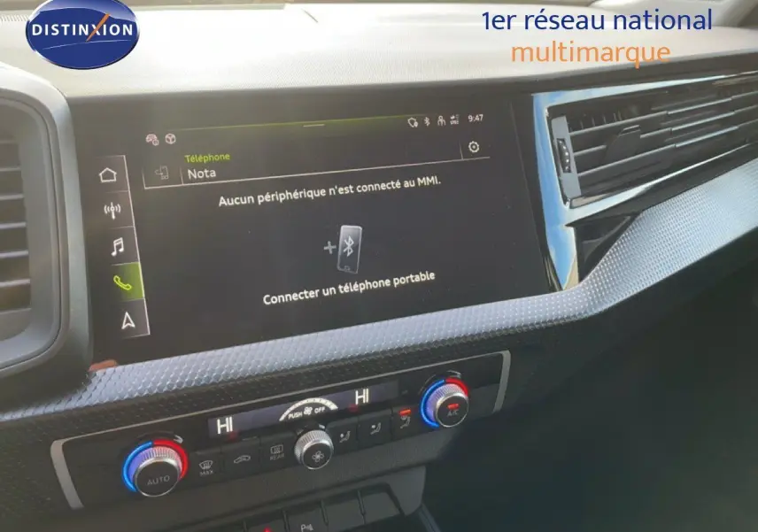 Tableau de bord de l'Audi A1 Sportback 2023 en blanc glacier, affichant l'écran tactile central et commandes climatisation.