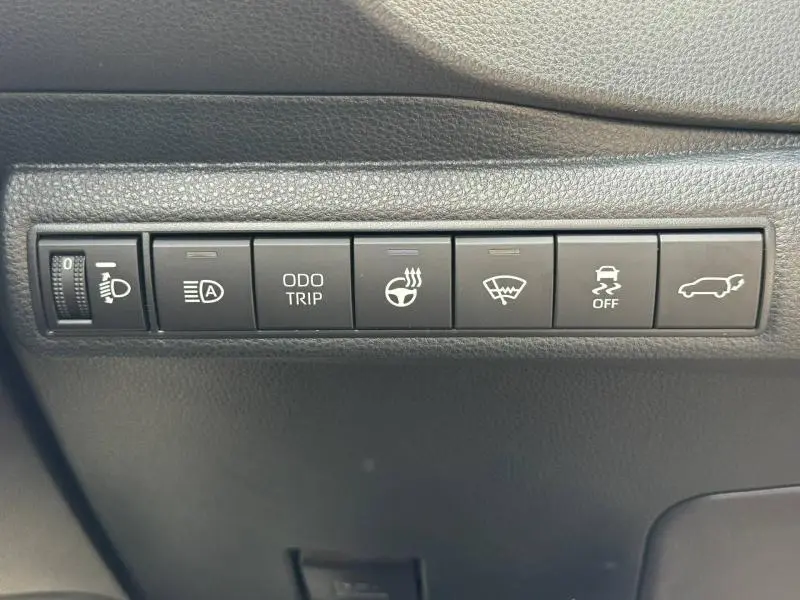 Gros plan sur la rangée de boutons de commande noirs avec icônes blanches dans l'habitacle d'une Toyota Corolla noire.