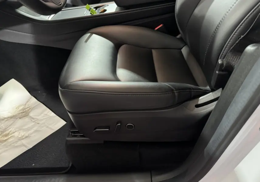 Gros plan sur le siège avant droit en cuir noir du Tesla Model Y blanc, avec commandes électriques visibles.