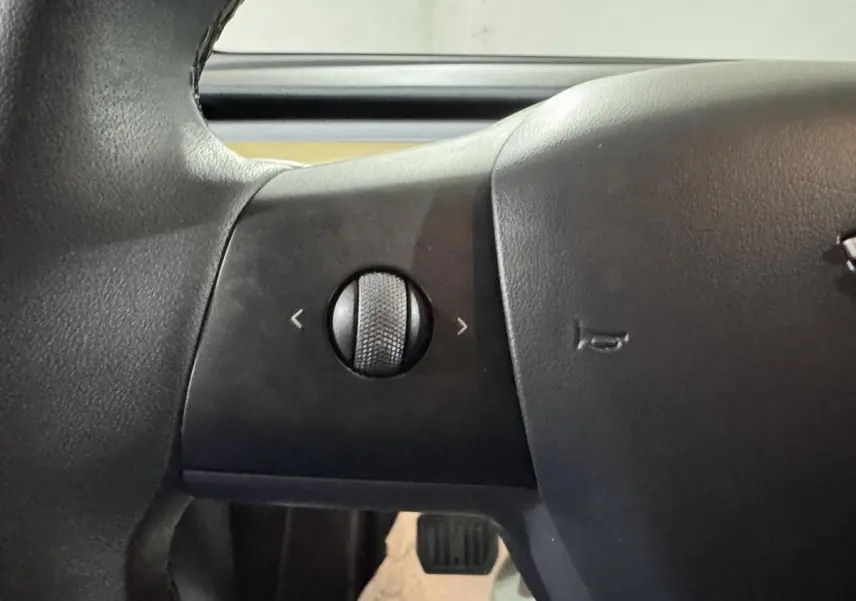 Gros plan sur la molette de réglage sur le côté gauche du volant noir d’un Tesla Model Y blanc.