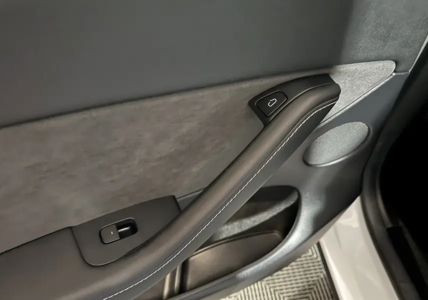 Détail de la porte intérieure côté conducteur d’une Tesla Model Y blanche, avec poignée noire et bouton de verrouillage.