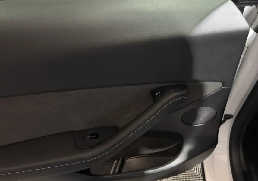 Gros plan sur la porte avant droite blanche d’un Tesla Model Y 2022, avec garniture noire et poignée intégrée.